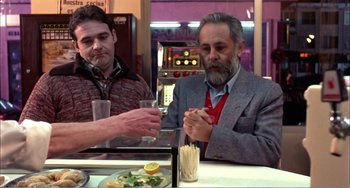 Movie still from “What Have I Done to Deserve This?” (1984), directed by Pedro Almodóvar – Two men sitting at a table in front of a plate of food; Medium shot, Low angle