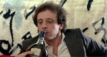 Movie still from “What Have I Done to Deserve This?” (1984), directed by Pedro Almodóvar – A man holding a bottle of wine in his hand; Close Up shot, Low angle