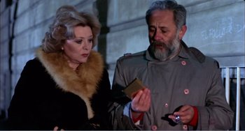 Movie still from “What Have I Done to Deserve This?” (1984), directed by Pedro Almodóvar – An older man and a woman looking at a book; Medium shot, High angle