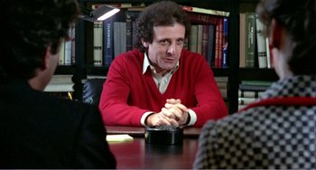 Movie still from “What Have I Done to Deserve This?” (1984), directed by Pedro Almodóvar – A man sitting at a table in front of a book shelf; Medium shot, Over the shoulder angle