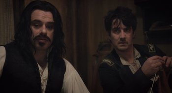 Movie still from “What We Do in the Shadows” (2014), directed by Taika Waititi – Two men standing next to each other in front of a wall; Medium shot, Over the shoulder angle