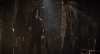 Movie still from “What We Do in the Shadows” (2014), directed by Taika Waititi – A man standing in a cave holding a stick; Wide shot, Low angle