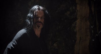 Movie still from “What We Do in the Shadows” (2014), directed by Taika Waititi – A man with long black hair standing next to a tree; Close Up shot, Over the shoulder angle