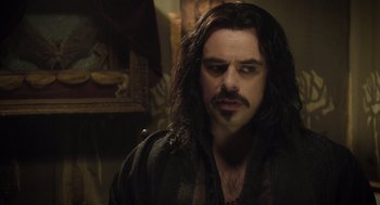 Movie still from “What We Do in the Shadows” (2014), directed by Taika Waititi – A man with long black hair and a mustache; Close Up shot, Over the shoulder angle