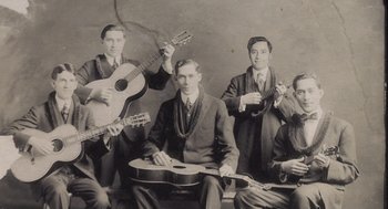 Movie still from “What We Do in the Shadows” (2014), directed by Taika Waititi – A group of men sitting next to each other holding instruments; Medium shot, Low angle