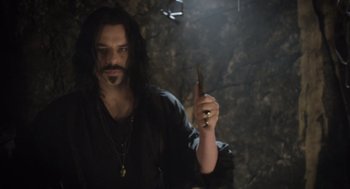 Movie still from “What We Do in the Shadows” (2014), directed by Taika Waititi – A man with long black hair holding a knife in his hand; Medium shot, High angle