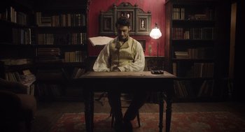 Movie still from “What We Do in the Shadows” (2014), directed by Taika Waititi – A man sitting at a table in a room; Medium shot, Low angle