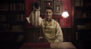 Movie still from “What We Do in the Shadows” (2014), directed by Taika Waititi – A man in a white shirt is holding up a piece of paper; Medium shot, High angle