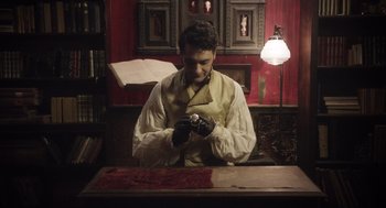 Movie still from “What We Do in the Shadows” (2014), directed by Taika Waititi – A man wearing a white shirt and black gloves; Medium shot, High angle