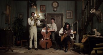 Movie still from “What We Do in the Shadows” (2014), directed by Taika Waititi – A group of men playing musical instruments in a room; Wide shot, Low angle