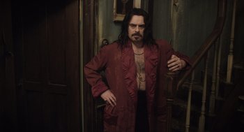 Movie still from “What We Do in the Shadows” (2014), directed by Taika Waititi – A man in a red robe standing next to a door; Medium shot, Over the shoulder angle