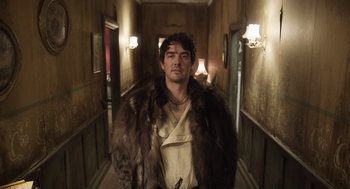 Movie still from “What We Do in the Shadows” (2014), directed by Taika Waititi – A man wearing a fur coat standing in a hallway; Medium shot, Low angle
