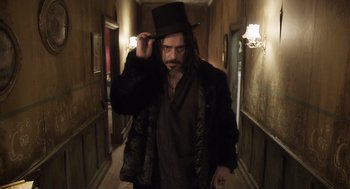 Movie still from “What We Do in the Shadows” (2014), directed by Taika Waititi – A man in a top hat in a dark hallway; Medium shot, Over the shoulder angle