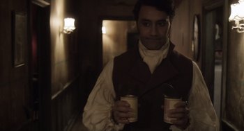 Movie still from “What We Do in the Shadows” (2014), directed by Taika Waititi – A man holding two cups of coffee in a dark room; Medium shot, Over the shoulder angle