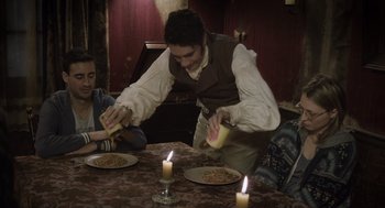 Movie still from “What We Do in the Shadows” (2014), directed by Taika Waititi – A man standing at a dinner table preparing a meal; Medium shot, High angle