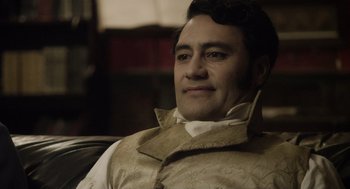 Movie still from “What We Do in the Shadows” (2014), directed by Taika Waititi – A person sitting in a chair wearing a vest; Close Up shot, Over the shoulder angle