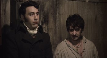 Movie still from “What We Do in the Shadows” (2014), directed by Taika Waititi – Two men standing next to each other in front of a brick wall; Medium shot, High angle