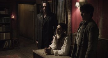 Movie still from “What We Do in the Shadows” (2014), directed by Taika Waititi – A group of men standing around a wooden table; Medium shot, Over the shoulder angle