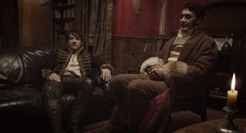 Movie still from “What We Do in the Shadows” (2014), directed by Taika Waititi – A group of men sitting on a couch in a room; Medium shot, Low angle