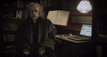Movie still from “What We Do in the Shadows” (2014), directed by Taika Waititi – An old man sitting in front of a laptop computer; Medium shot, High angle