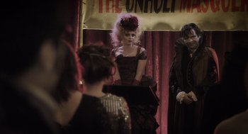 Movie still from “What We Do in the Shadows” (2014), directed by Taika Waititi – A woman in a black dress and a red flower in her hair; Medium shot, Over the shoulder angle