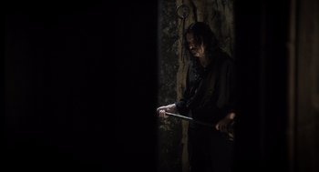 Movie still from “What We Do in the Shadows” (2014), directed by Taika Waititi – A man holding a stick in a dark room; Medium shot, Over the shoulder angle