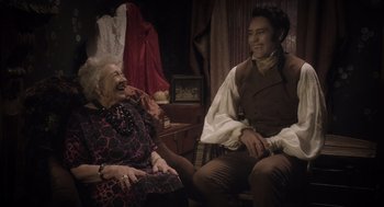 Movie still from “What We Do in the Shadows” (2014), directed by Taika Waititi – An old woman and a young man sitting on a chair; Medium shot, Over the shoulder angle