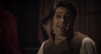 Movie still from “What We Do in the Shadows” (2014), directed by Taika Waititi – A man in a brown vest and a brown tie smiling; Close Up shot, High angle