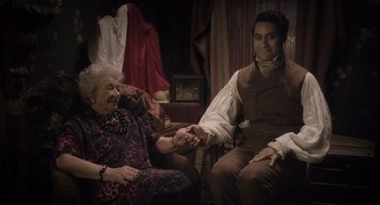 Movie still from “What We Do in the Shadows” (2014), directed by Taika Waititi – An old woman and a young man holding hands; Medium shot, Over the shoulder angle