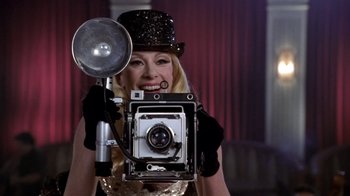Movie still from “What Women Want” (2000), directed by Nancy Meyers – A woman holding an old fashioned camera in a hat; Close Up shot, Low angle