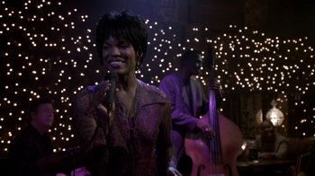 Movie still from “What Women Want” (2000), directed by Nancy Meyers – A woman singing into a microphone in front of a man playing a double bass; Medium shot, High angle