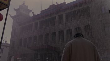 Movie still from “What Women Want” (2000), directed by Nancy Meyers – A man standing in the rain in front of an old building; Wide shot, Low angle