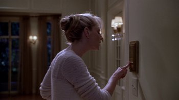 Movie still from “What Women Want” (2000), directed by Nancy Meyers – A woman in a white sweater is turning on a light switch; Medium shot, High angle