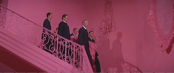 Movie still from “What a Way to Go!” (1964), directed by J. Lee Thompson – A group of men standing on top of a pink staircase; Wide shot, Low angle