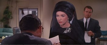 Movie still from “What a Way to Go!” (1964), directed by J. Lee Thompson – A woman in a black dress holding a card; Close Up shot, Over the shoulder angle