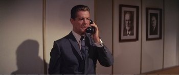 Movie still from “What a Way to Go!” (1964), directed by J. Lee Thompson – A man talking on a phone while wearing a suit and tie; Medium shot, Low angle