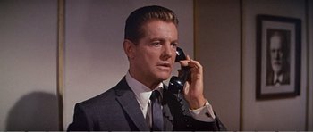 Movie still from “What a Way to Go!” (1964), directed by J. Lee Thompson – A man talking on a phone while wearing a suit and tie; Close Up shot, Low angle