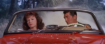 Movie still from “What a Way to Go!” (1964), directed by J. Lee Thompson – A man and a woman sitting in the back seat of a red car; Medium shot, Low angle