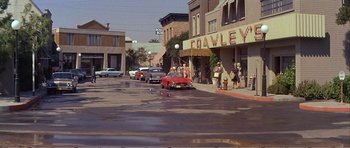 Movie still from “What a Way to Go!” (1964), directed by J. Lee Thompson – A red car driving down a street next to buildings; Extreme Wide shot, High angle