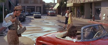 Movie still from “What a Way to Go!” (1964), directed by J. Lee Thompson – Two women walk down the street while a red car drives by; Wide shot, High angle