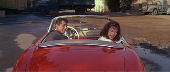 Movie still from “What a Way to Go!” (1964), directed by J. Lee Thompson – A man and a woman sitting in the back seat of a red car; Medium shot, High angle