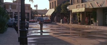 Movie still from “What a Way to Go!” (1964), directed by J. Lee Thompson – A man is walking down the street in the rain; Wide shot, Over the shoulder angle