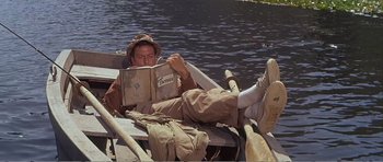 Movie still from “What a Way to Go!” (1964), directed by J. Lee Thompson – A man reading a book while sitting in a boat; Wide shot, High angle