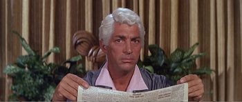 Movie still from “What a Way to Go!” (1964), directed by J. Lee Thompson – A man holding a newspaper while looking at the camera; Close Up shot, Low angle