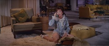 Movie still from “What a Way to Go!” (1964), directed by J. Lee Thompson – A woman sitting on the ground talking on a phone; Medium shot, High angle