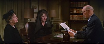 Movie still from “What a Way to Go!” (1964), directed by J. Lee Thompson – A woman sitting at a table with a sheet over her head; Medium shot, Over the shoulder angle