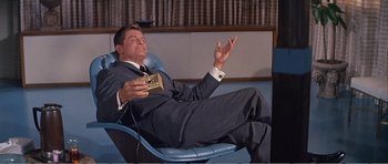 Movie still from “What a Way to Go!” (1964), directed by J. Lee Thompson – A man sitting in a chair holding a cell phone; Medium shot, High angle