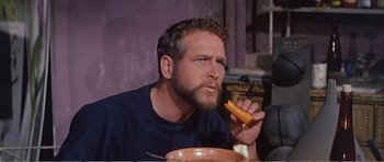 Movie still from “What a Way to Go!” (1964), directed by J. Lee Thompson – A man with a beard is eating a piece of food; Close Up shot, Over the shoulder angle