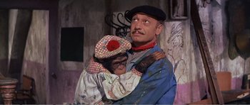 Movie still from “What a Way to Go!” (1964), directed by J. Lee Thompson – A man holding a monkey in his arms; Medium shot, Low angle