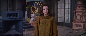 Movie still from “What a Way to Go!” (1964), directed by J. Lee Thompson – A woman in a brown sweater standing in front of a painting; Medium shot, Low angle
